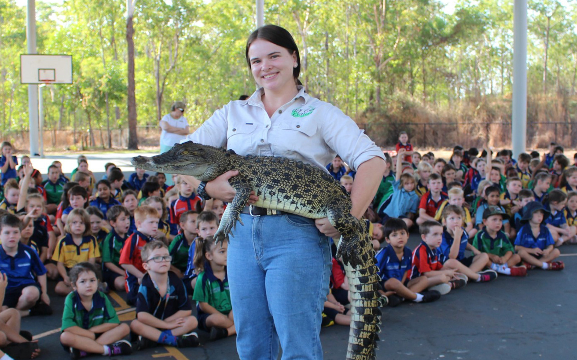 Top End Critters staff holding crocodile with students in background.